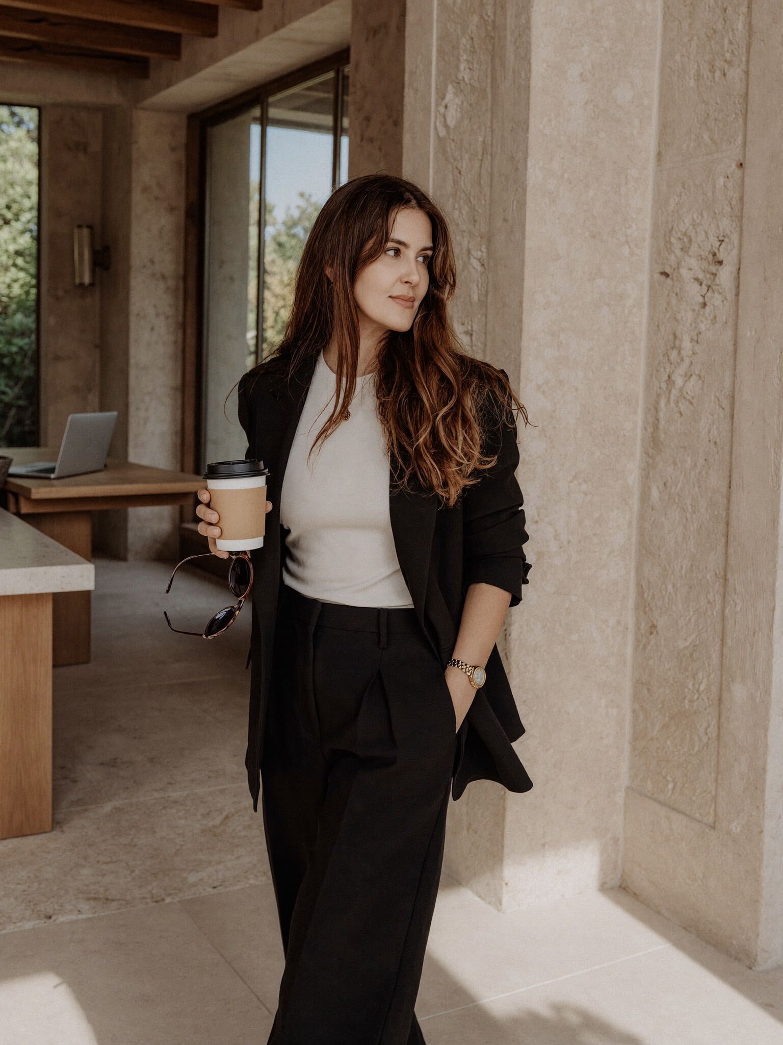 Nadine B., Founder of Meridio Partners, in a warm stone hallway holding a coffee